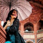 A cheerful woman with an umbrella enjoys the rain in New Delhi's architectural beauty.