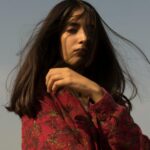 Stylish portrait of a woman in wind with long hair and red shirt outdoors.